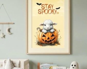May include: A framed wall art print featuring a fluffy white lamb sitting inside a carved orange jack-o'-lantern pumpkin. The background is a soft yellow with two black bats and the text STAY SPOOKY written in brown letters.