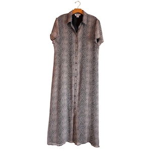 Könnte beinhalten: Ein langes, knöpfbares Kleid mit Leopardenmuster. Das Kleid hat kurze Ärmel und einen Kragen. Es hängt an einem Holzkleiderbügel.