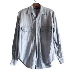 Peut inclure: Chemise bleu clair à manches longues avec deux poches de poitrine et une fermeture boutonnée. La chemise est en tissu clair et est suspendue à un cintre en bois. Elle a un col classique et des poignets boutonnés.