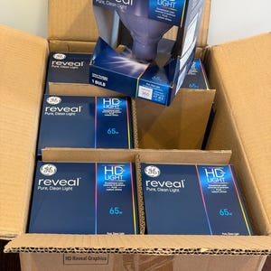 May include: A cardboard shipping box containing multiple GE Reveal HD Light indoor floodlight bulbs in dark blue packaging. Each box displays the text Reveal Pure, Clean Light, HD Light, and 65w. One bulb box is positioned upright on top.
