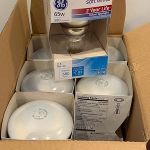 May include: A cardboard box containing multiple GE soft white indoor spotlight bulbs. Each bulb is 65 watts, 580 lumens, and labeled as a directional BR30. The packaging displays technical lighting facts, a 2-year life rating, and energy cost details.
