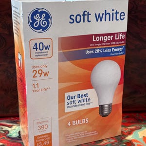 May include: A GE brand soft white light bulb box containing 4 bulbs. The packaging is white and orange with blue text, featuring a 40w incandescent replacement label, 29w energy usage, 390 lumens brightness, and a 1.1 year life rating.