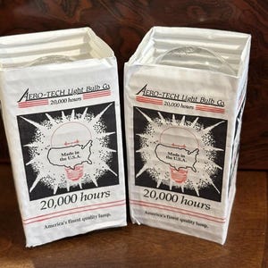 May include: Two white light bulb boxes with the text "AERO-TECH Light Bulb Co." and "20,000 hours." Each box features a graphic of a light bulb inside the U.S.A. and the text "Made in the U.S.A." and "America's finest quality lamp."