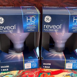 May include: Two boxes of GE Reveal HD+ Light 65 watt indoor floodlight bulbs. The boxes are blue and white with a picture of the bulb and the text "GE Reveal Pure, Clean Light" and "HD+ Light".