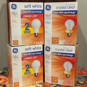 May include: Two packs of GE energy-efficient light bulbs. Each pack contains two bulbs and is labeled "soft white" and "crystal clear". The bulbs are 40 watt equivalent and use 28% less energy than traditional incandescent bulbs. The packaging also states that the bulbs have a longer life than traditional bulbs.