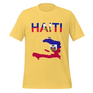 May include: Yellow t-shirt featuring the word "HAITI" in red, white, and blue letters. Below the text is a map of Haiti in red, blue, and white, with the Haitian coat of arms in the center. The shirt is made of a soft material.