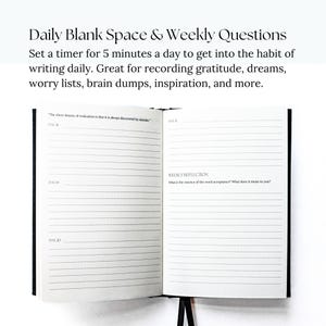 May include: A black and white journal with lined pages for daily writing prompts and weekly reflection questions. The text on the page reads "The sheer beauty of realization is that it is always discovered by mistake." and "What is the essence of the word acceptance? What does it mean to you?"