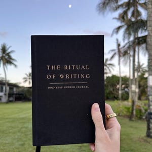 May include: A black journal with gold lettering that reads "The Ritual of Writing" and "One-Year Guided Journal".