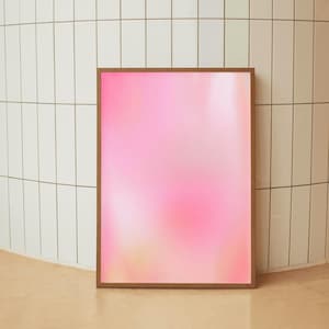 May include: A framed artwork with a soft pink and white gradient. The artwork is in a brown wooden frame and leans against a white tiled wall and a beige floor. The overall aesthetic is minimalist and modern.