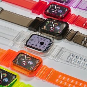 May include: Several Apple watches with transparent straps in a range of colours, such as purple, red, grey, and orange. The watch faces show the time and other details. The straps are made of a clear, flexible material.