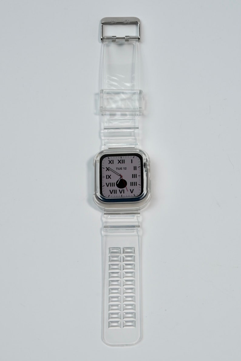 May include: A clear plastic watch band with a silver buckle and a clear plastic watch face with Roman numeral markings. The watch face displays the date "TUE 12".
