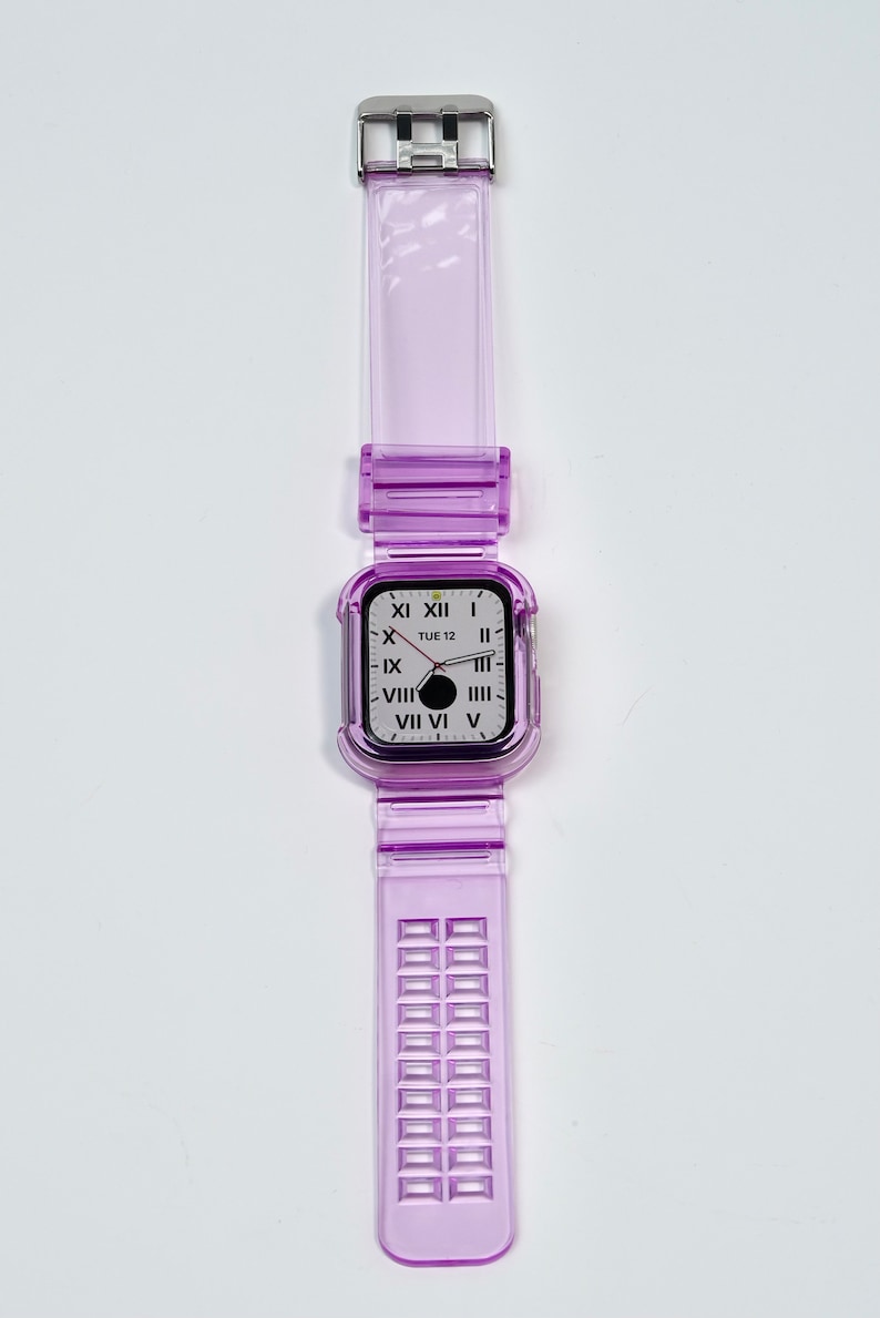 May include: A clear purple watch band with a silver buckle and a clear purple case with a white watch face that says "TUE 12" and has Roman numerals.