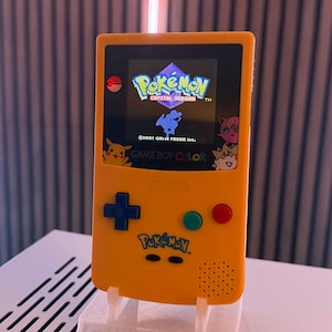 Puede incluir: Una taza de cerámica blanca con asa negra y el texto "But First, Coffee" en negrita negra. La taza se encuentra sobre un fondo borroso, sugiriendo un ambiente acogedor.