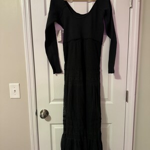 May include: A black long-sleeved maxi dress with a lace overlay and a scoop neckline. The dress has a fitted bodice and a flowing skirt.