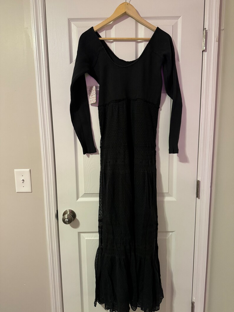 May include: A black long-sleeved maxi dress with a lace overlay and a scoop neckline. The dress has a fitted bodice and a flowing skirt.