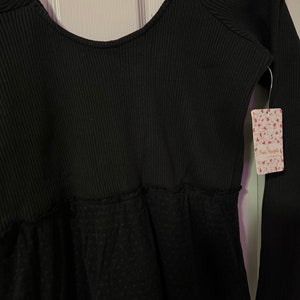 May include: Black long-sleeve top with a scoop neck and a lace bottom. The top has a ribbed texture and a Free People tag attached.
