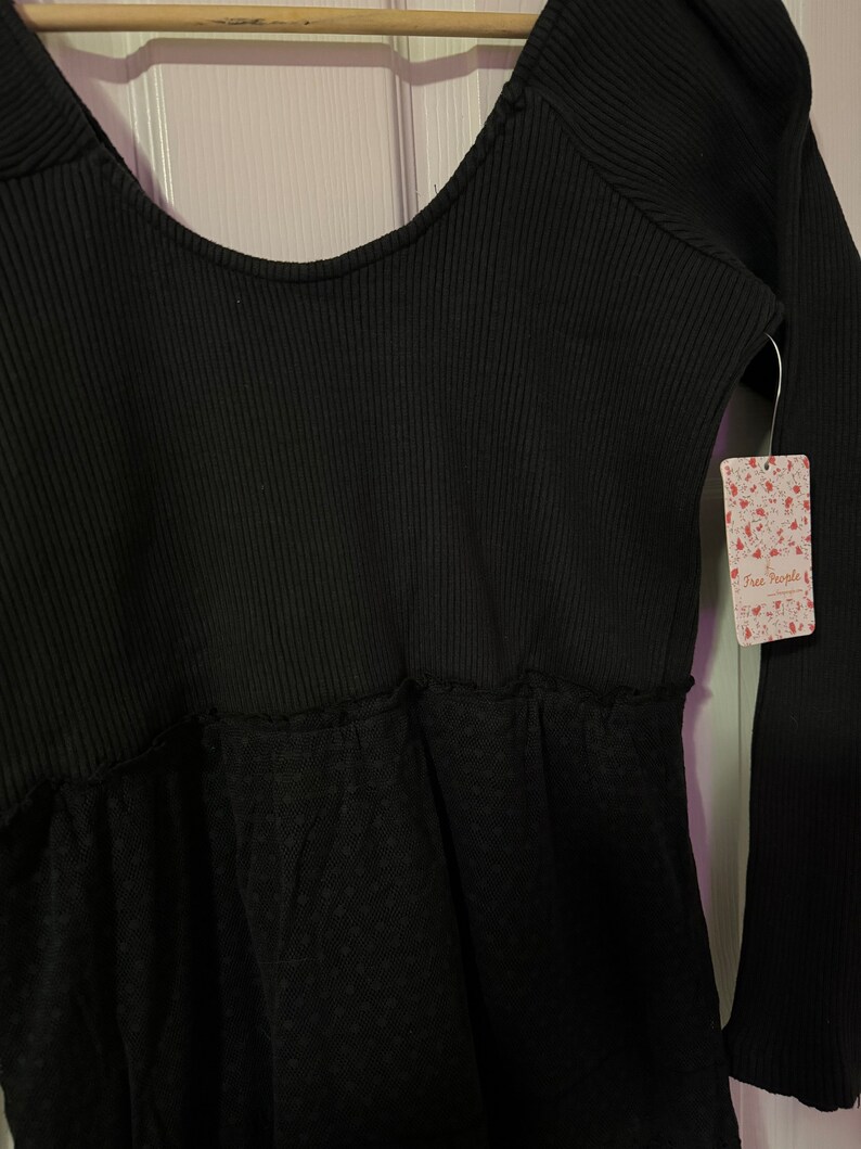 May include: Black long-sleeve top with a scoop neck and a lace bottom. The top has a ribbed texture and a Free People tag attached.