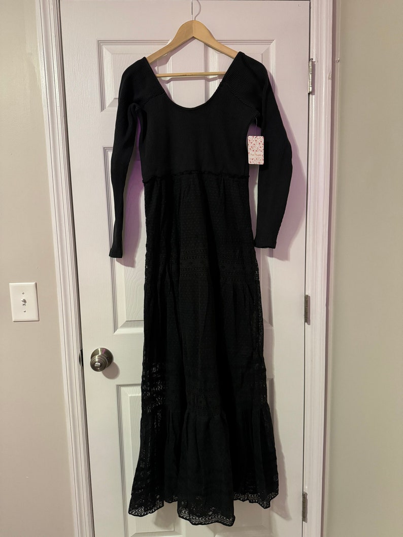 May include: Black maxi dress with long sleeves and a lace overlay. The dress has a scoop neckline and a tiered skirt.