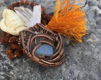 May include: A copper wire wrapped pendant with a blue opal stone. The pendant is surrounded by a white crystal, brown beads, and a bright orange tassel.