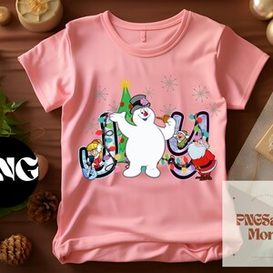 May include: Pink t-shirt with a snowman, a Christmas tree, and lights that spell out "Joy".