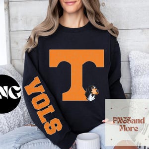 May include: Black sweatshirt with orange "VOLS" lettering on the sleeve and a large orange "T" on the front. The "T" has a small black and white dog graphic on the right side.