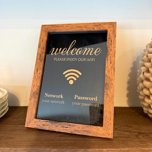 Może przedstawiać: Oprawiony znak z ciemnym tłem. Zawiera napis "welcome" złotym pismem, a poniżej "PLEASE ENJOY OUR WIFI". Znak zawiera również symbol Wi-Fi i prosi o podanie szczegółów sieci i hasła.