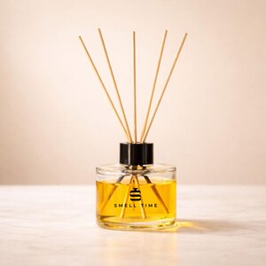 May include: A clear glass aromatherapy diffuser with a black cap and wooden reeds. The bottle contains a yellow liquid and the text "SMELL TIME" is printed on the front. The diffuser is on a white surface.