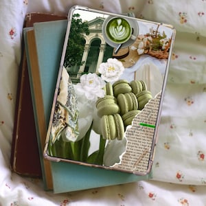 May include: A phone case featuring a collage of images. The collage includes a green building, white flowers, green macarons, a cup of green tea, and a straw hat. The background is a book with text.