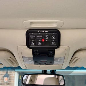 May include: Black AUXBEAM light control panel with various labelled buttons for roof light, light bar, side, rear, hood, flood, and fog lights. The panel is mounted on a vehicle's ceiling, above the rearview mirror.