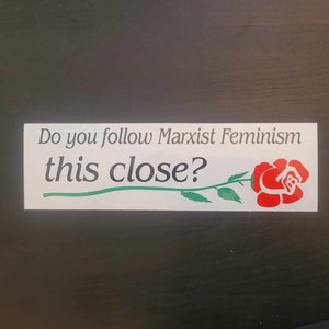 Op de afbeelding: Witte sticker met de tekst "Do you follow Marxist Feminism this close?" en een rode roos met een groene steel en bladeren.
