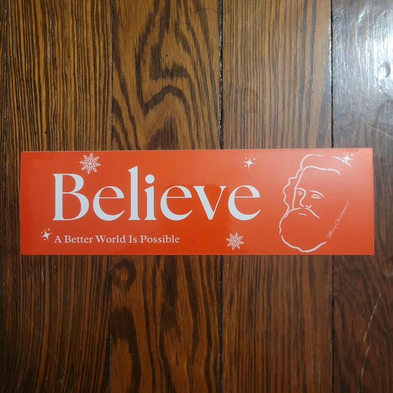 Puede incluir: Una pegatina rectangular roja con texto blanco que dice "Believe" y "A Better World Is Possible". Una imagen estilizada de Santa Claus est&aacute; en el lado derecho de la pegatina.
