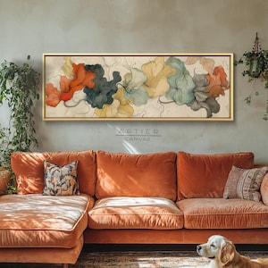 Puede incluir: Una pintura floral abstracta enmarcada, con formas rojas, turquesas, amarillas y grises, cuelga sobre un sofá de terciopelo naranja. Un perro golden retriever descansa sobre la alfombra estampada frente al sofá. La obra está firmada "ARTIER CANVAS".