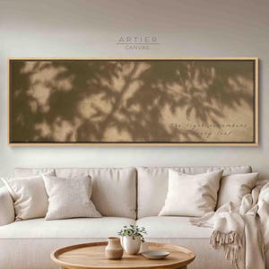 May include: A rectangular horizontal canvas wall art piece featuring a warm beige background with dark brown shadows of tree leaves cast across the surface. The text "The light remembers every leaf" is printed in the lower right corner of the canvas.