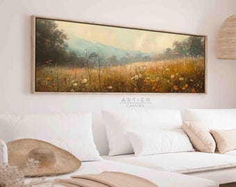 Puede incluir: Una impresión en lienzo horizontal y larga de una escena de paisaje con un campo de flores silvestres en primer plano y una cordillera en el fondo. El cielo es de un azul suave con un toque de rosa y naranja. La impresión está enmarcada en un marco de madera claro.