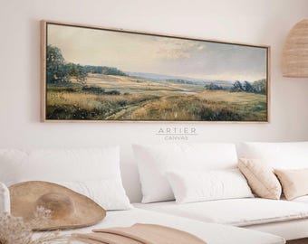 May include: A long, horizontal landscape painting in a wooden frame, depicting a field with a winding path leading to a distant horizon. The painting is hung above a white sofa with cushions and a throw blanket.