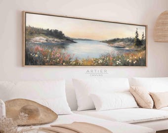 Puede incluir: Una pintura de lienzo larga y horizontal que representa una escena de lago con una orilla de árboles y flores silvestres. El cielo es de un azul suave y pálido con un toque de naranja en la distancia. El agua es de un azul claro y refleja el cielo. La pintura está enmarcada en un marco de madera claro.