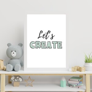 May include: A white framed print with the text "Let's CREATE" in black and green lettering. The print is sitting on a white shelf with a grey teddy bear, wooden toys, and a potted plant.