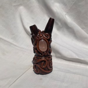 Peut inclure: Une petite sculpture en céramique artisanale avec un cristal de quartz rose incrusté au centre. La sculpture est de couleur brune et présente un design détaillé et complexe.