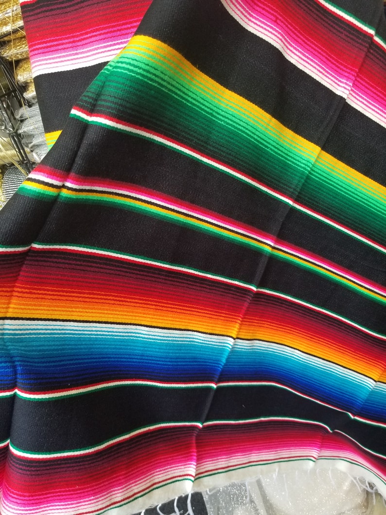 May include: A colorful Mexican blanket with stripes of red, pink, white, yellow, orange, blue, green, and black. The blanket is folded in half and has a fringe on the bottom.