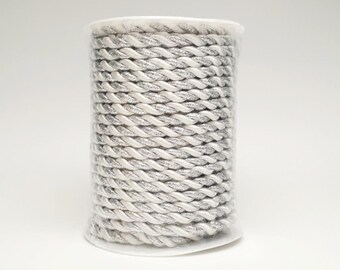 May include: A spool of white and silver twisted cord. The cord is tightly wound, creating a textured surface. The silver threads add a subtle sparkle to the cord. This decorative cord is suitable for various craft projects.