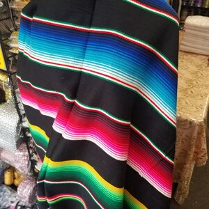 May include: A black and colorful striped Mexican blanket with a fringe. The blanket is folded in half and is made of a soft, woven fabric.