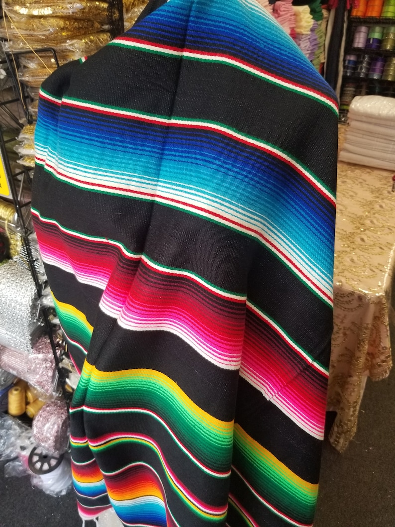 May include: A black and colorful striped Mexican blanket with a fringe. The blanket is folded in half and is made of a soft, woven fabric.