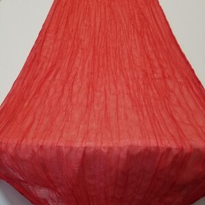 May include: Red crinkled table runner. The runner is made of a lightweight fabric and has a textured, wrinkled appearance.