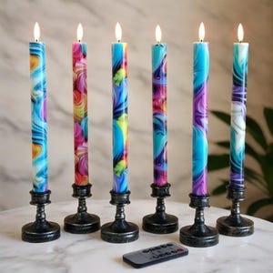 May include: Six colorful swirl-patterned candles with lit flames, each set in a black metal candlestick. The candles display a mix of blue, pink, yellow, and purple hues. A remote control is placed in front of the candles.