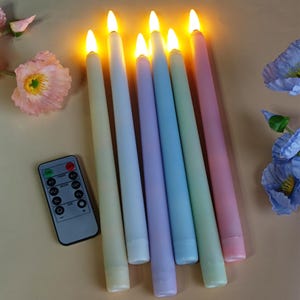 May include: A collection of seven pastel-coloured LED taper candles with a remote control. The candles are arranged diagonally, each emitting a warm, flickering light. The colours include light green, blue, purple, and pink. The remote control is on the left.