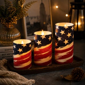 Könnte beinhalten: Drei zylindrische LED-Stumpenkerzen mit einem aufgemalten amerikanischen Flaggendesign, bestehend aus einem blauen Feld mit weißen Sternen sowie roten und weißen Streifen. Jede Kerze strahlt oben ein warmes Licht aus und erzeugt einen realistischen Flammeneffekt.
