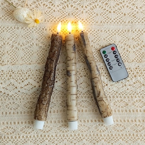 Puede incluir: Tres velas LED con efecto madera de corteza y abedul, cada una con una luz ámbar parpadeante. Las velas tienen bases blancas y se controlan con un mando a distancia. Altura aproximada 20 cm.
