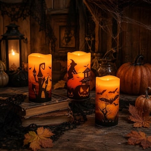 Peut inclure: Trois bougies LED cylindriques à lumière orange chaude. L'une présente une maison hantée et des chauves-souris, une autre une sorcière sur un balai avec une citrouille, et la troisième un arbre avec des chauves-souris et des citrouilles.