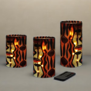 Może przedstawiać: Zestaw trzech cylindrycznych, dekoracyjnych świeczników z pomarańczowym, czarnym i żółtym wzorem. Świeczniki mają powtarzający się wzór i są podświetlane od wewnątrz. Pilot znajduje się przed świecznikami.