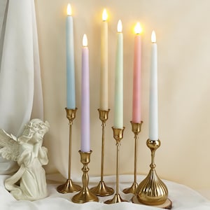 May include: A selection of pastel-coloured LED taper candles in blue, purple, yellow, green, pink, and white. Each candle sits in a gold-coloured candlestick holder. The candles are lit, creating a warm atmosphere.